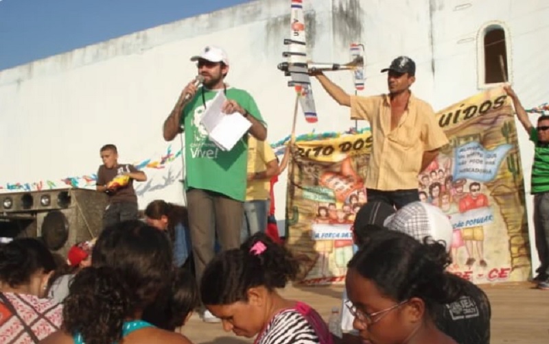 Zé Maria do Tomé (de camisa amarela, segurando um avião) durante protesto em 2008, em Limoeiro do Norte (CE), contra pulverização aérea de agrotóxicos. Na foto Zé Maria está em um palanque acompanhado de maus três pessoas. A frente do palanque há homens e mulheres ouvindo o discurso. (Foto:Arquivo/Deputado Renato Roseno)